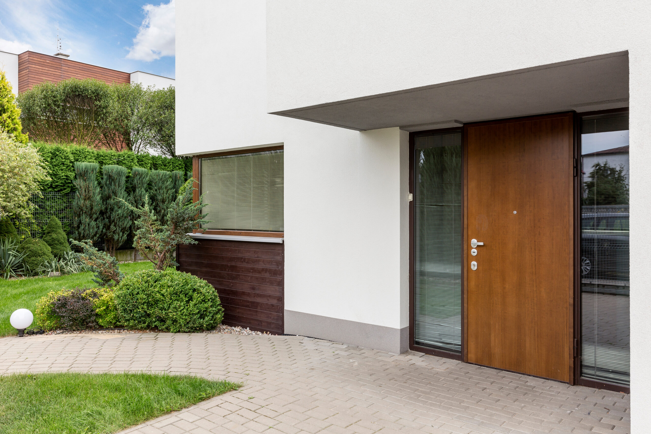 Wooden entrance door to modern white house with paving footpath and backside garden